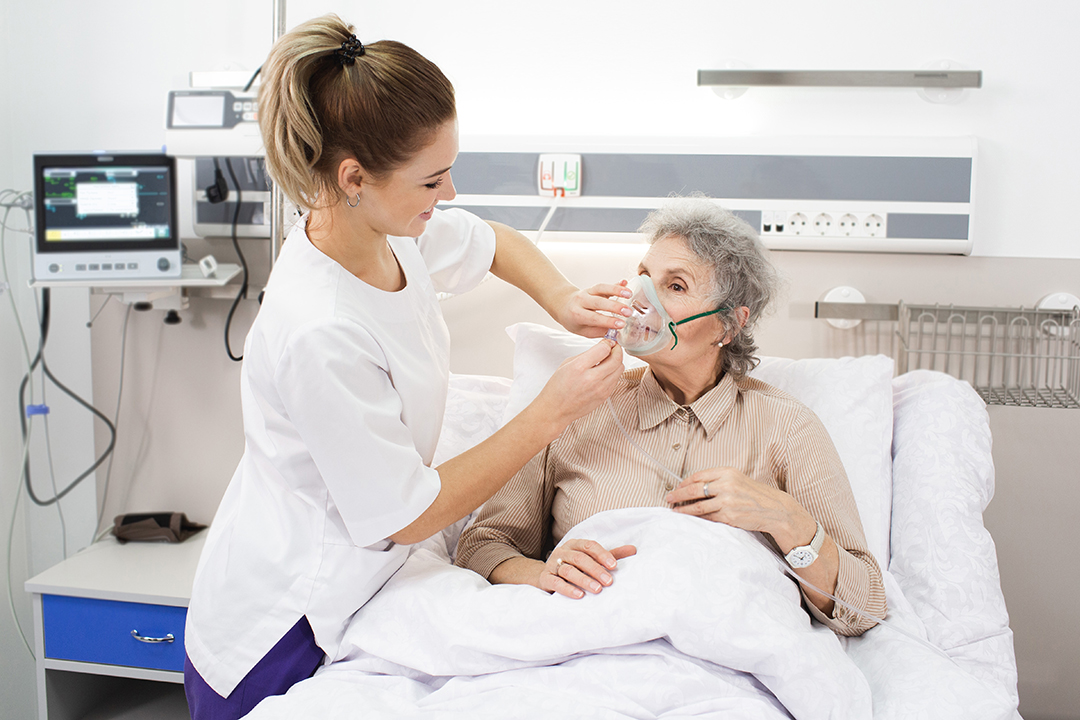 A nurse provides care to an elderly woman using a breathing mask in a medical clinic environment.